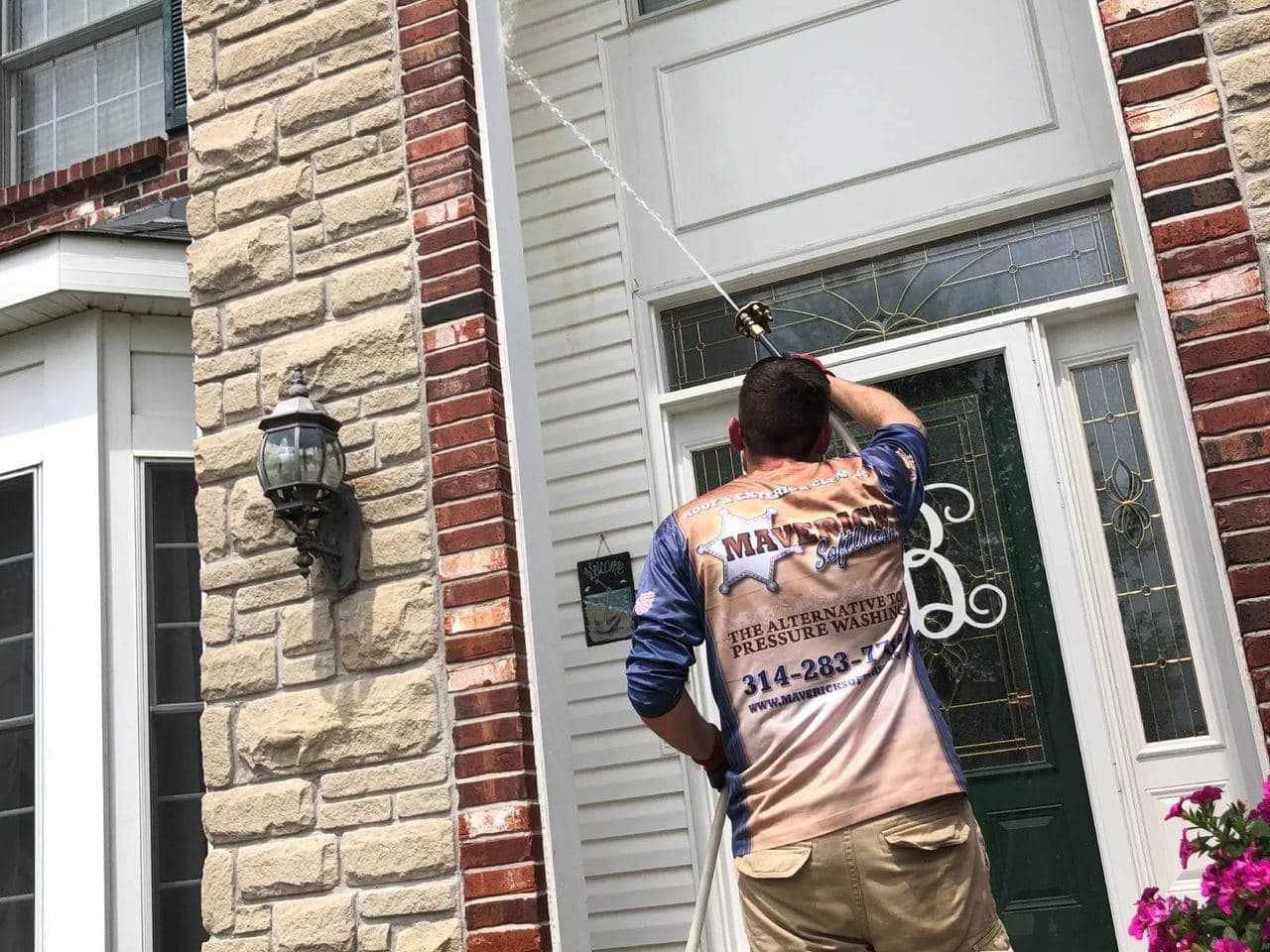 A technician in a Maverick SoftWash jersey softwashing a front entry